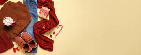 Set of children's clothes with Christmas gift and cup of hot chocolate on color background with space for textの写真素材