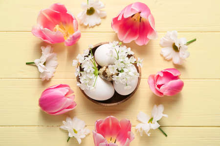 Composition with Easter eggs and spring flowers on color wooden background