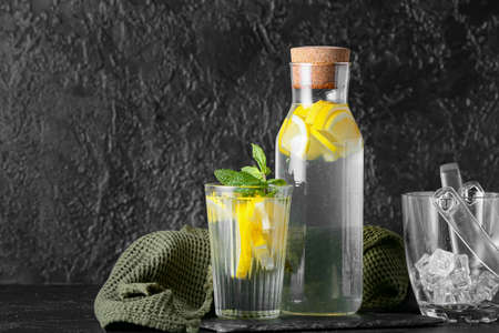 Bottle and glass of tasty cold lemonade on dark background