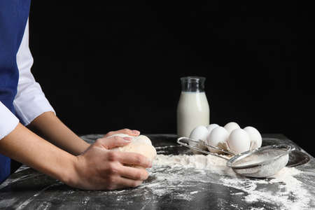 Woman kneading dough on dark background