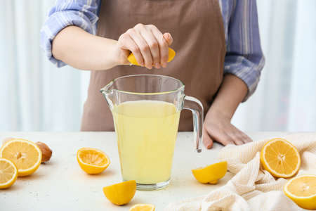 Woman squeezing lemon into jug at table in kitchen, closeupの写真素材