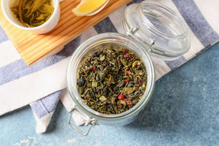 Jar of dry green tea on color background
