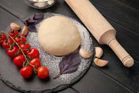 Board with dough and ingredients for preparing pizza on dark wooden background, closeupの写真素材