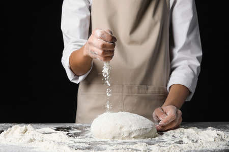 Woman sprinkling dough with flour on dark backgroundの写真素材