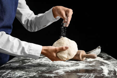 Woman sprinkling dough with flour on dark backgroundの写真素材