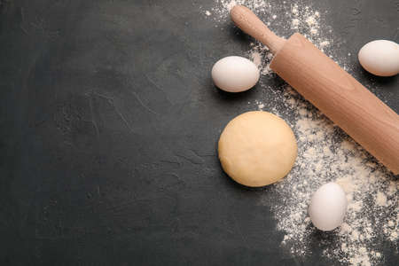 Fresh dough with eggs and rolling pin on dark background