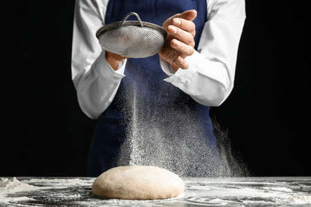 Woman sieving flour on dough on dark backgroundの写真素材