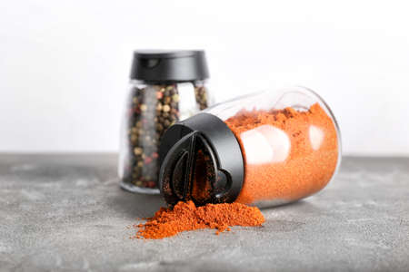 Jars with red pepper powder and peppercorns on table