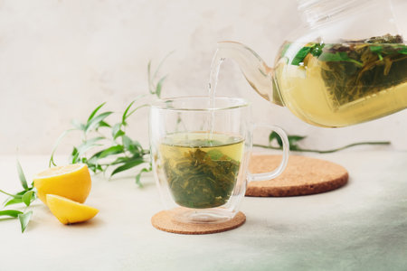 Pouring of green tea from teapot into cup on light backgroundの写真素材