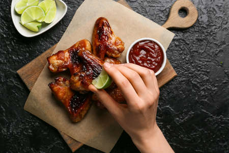 Woman squeezing lime on roasted chicken wings on dark backgroundの写真素材