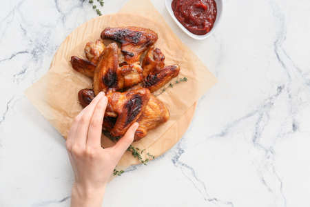 Woman eating roasted chicken wings on light backgroundの写真素材