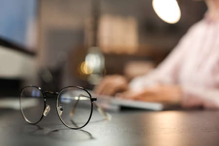 Stylish eyeglasses on table of working woman late in eveningの写真素材