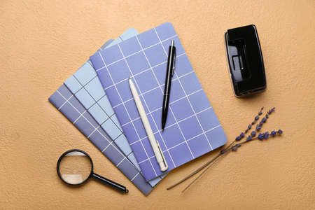 Notebooks, pens, hole puncher and magnifier on color background