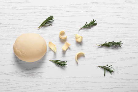Composition with fresh dough, rosemary and butter on light wooden background