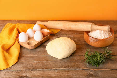 Fresh dough, flour, eggs and rosemary on wooden background