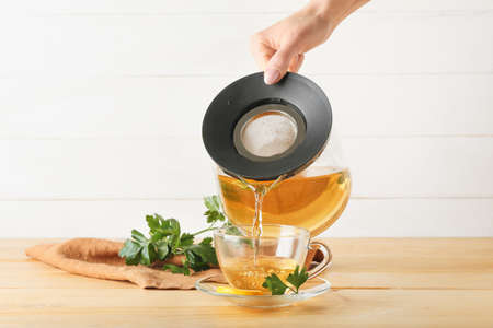Woman pouring hot tea from teapot into cup on wooden backgroundの写真素材