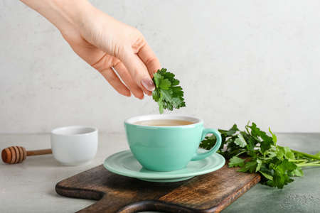 Woman preparing hot tea with parsley on light backgroundの写真素材