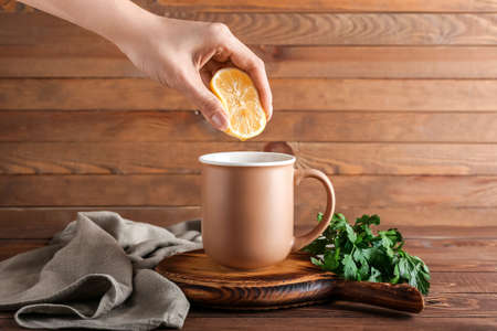 Woman squeezing lemon juice into cup of hot tea with parsley on wooden backgroundの写真素材