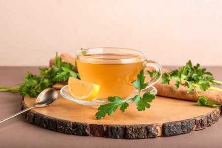 Board with cup of hot tea, parsley and lemon on color backgroundの写真素材