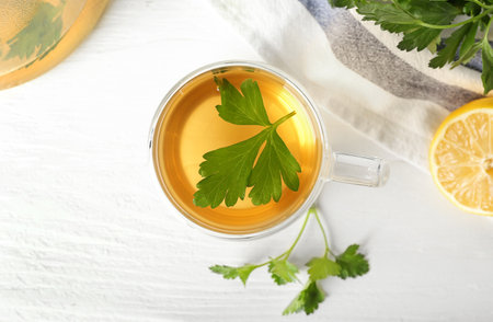 Cup of hot tea, parsley and lemon on light wooden backgroundの写真素材