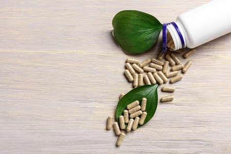 Bottle with pills and leaves on light wooden background, closeupの写真素材