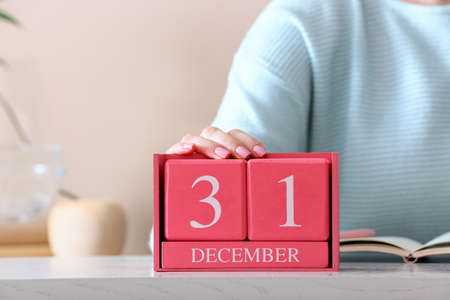 Woman holding cube calendar with date DECEMBER 31 on table in room, closeupの写真素材