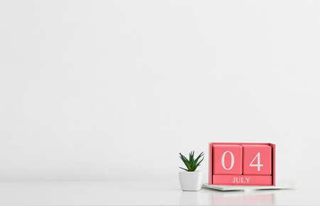 Cube calendar with date JULY 4, houseplant and notebooks on light background
