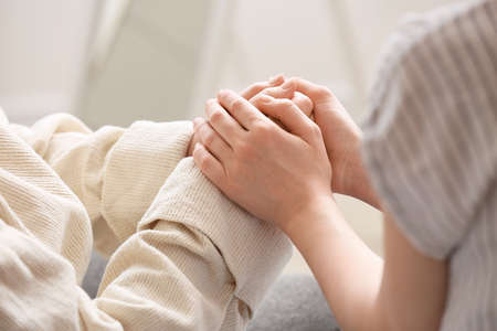 Young woman holding hands of her grandmother at home