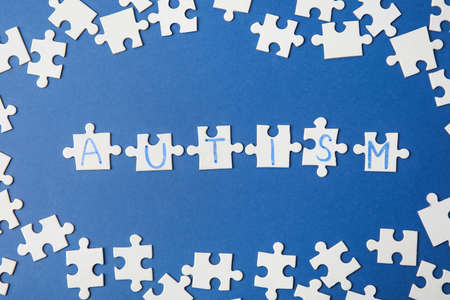 Word AUTISM made of puzzles on color background