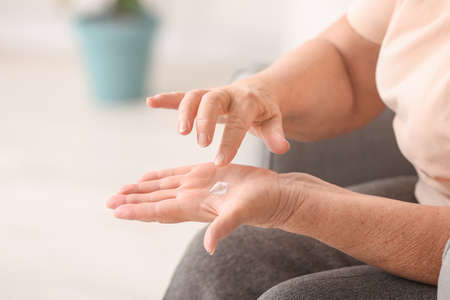 Elderly woman applying cosmetic cream onto her hands at homeの写真素材