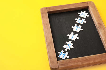 Word AUTISM made of puzzles and chalk board on color background