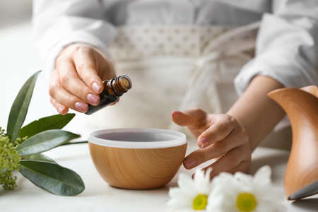 Woman adding essential oil to aroma diffuser on table