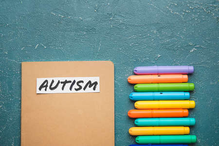 Notebook with word AUTISM and markers on grunge background