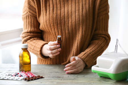 Woman with bottle of essential oil and nebulizer on tableの写真素材
