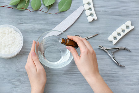 Manicure master adding essential oil to water in bowl on table, top viewの写真素材