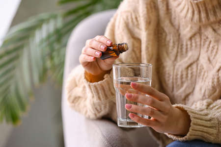 Woman adding essential oil to water in glass at homeの写真素材