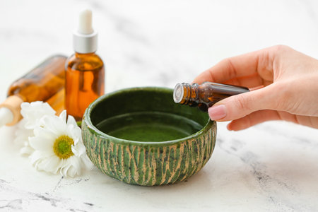 Woman adding essential oil to water in bowl on white backgroundの写真素材