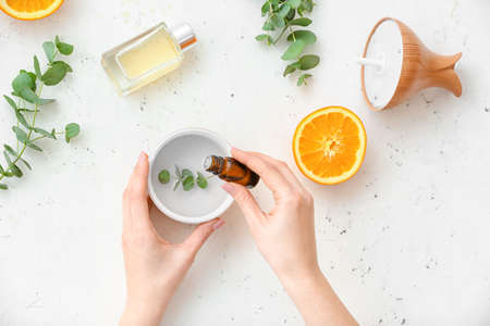 Woman adding essential oil to aroma diffuser on white background, top viewの写真素材