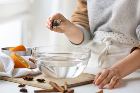 Woman adding essential oil to water in bowl on tableの写真素材