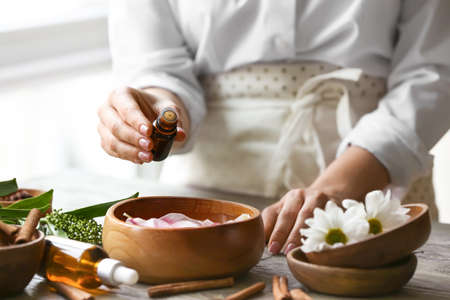 Woman adding essential oil to water in bowl on tableの写真素材