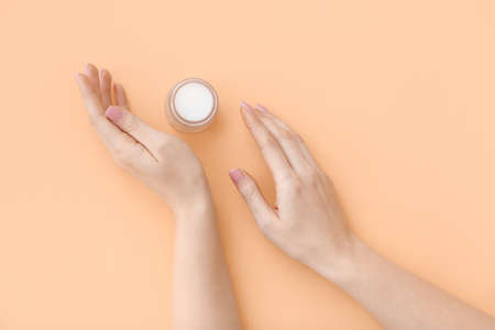 Female hands with jar of cosmetic cream on color backgroundの写真素材