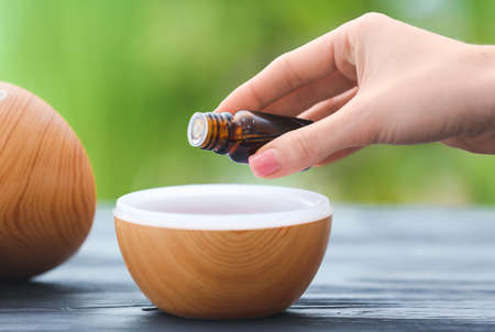 Woman adding essential oil to aroma diffuser on tableの写真素材