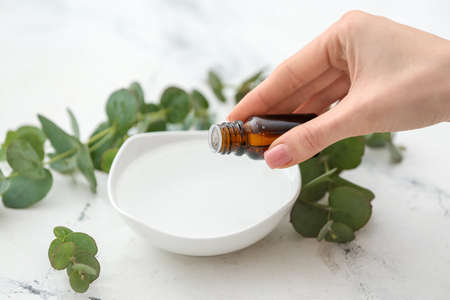 Woman adding essential oil to water in bowl on white backgroundの写真素材
