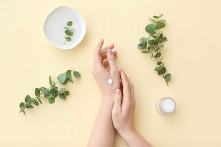 Woman applying cosmetic cream onto hands against light backgroundの写真素材