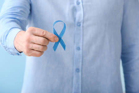 Man with blue ribbon on color background, closeup. Prostate cancer awareness concept