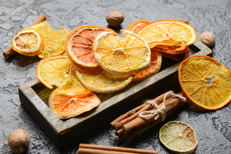 Dried citrus fruits, nutmegs and cinnamon on dark background