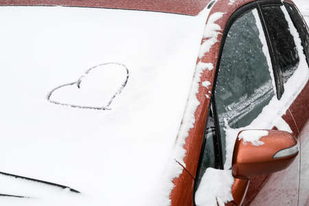 Heart drawn on snow covered carの写真素材