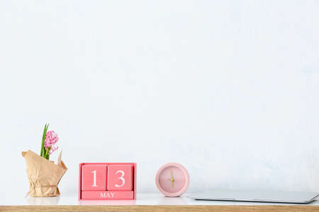 Cube calendar with date MAY 13, alarm clock and flowers on table in room