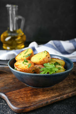 Bowl of tasty baked potatoes with parsley on dark backgroundの写真素材