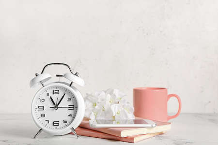 Composition with alarm clock, notebooks, mobile phone and cup on light background